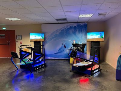 Simulateur de surf VR installé en salle avec écrans et décor de vague